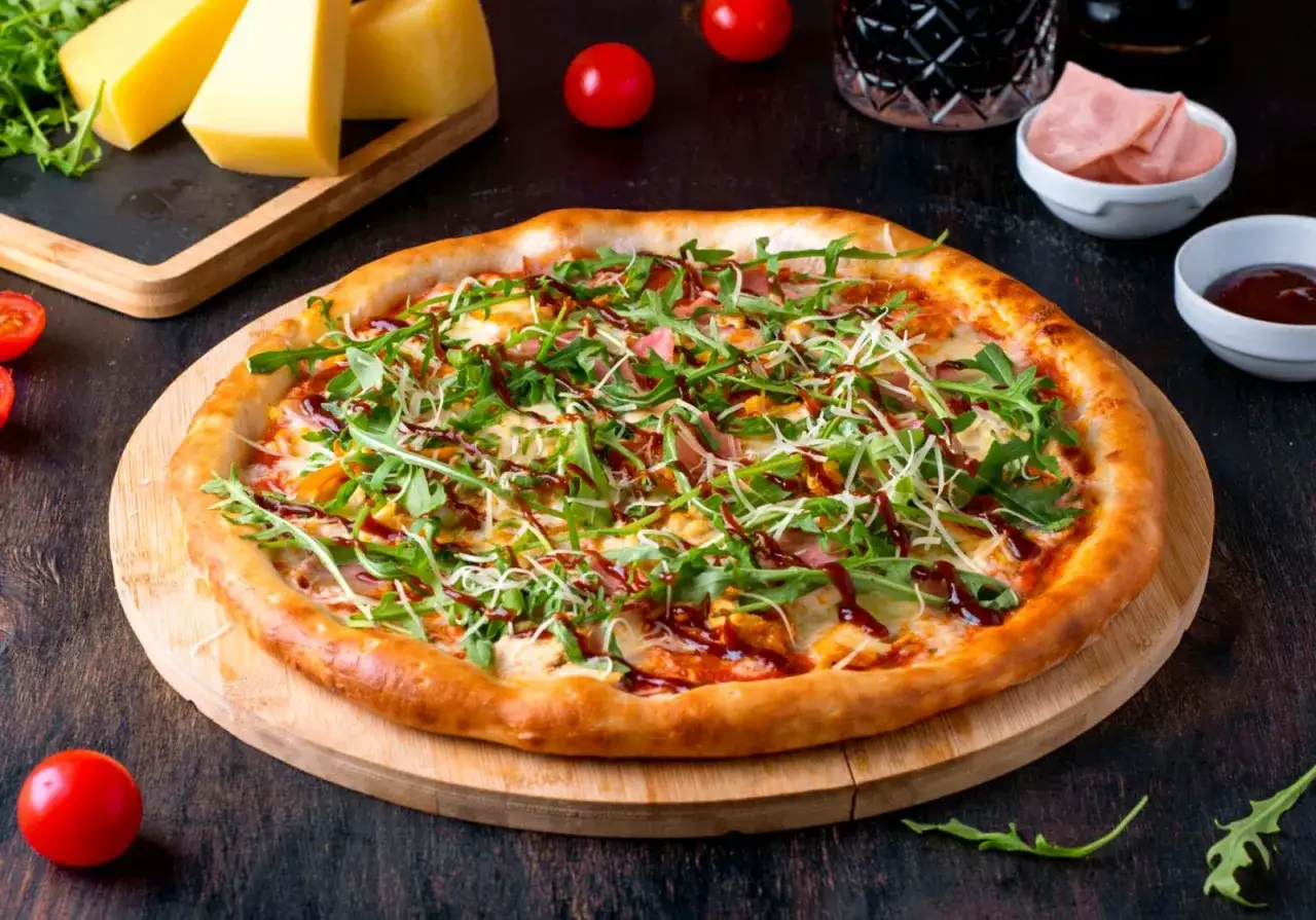 Apetyczna pizza z rukolą i szynką, posypana startym parmezanem do pizzy, polana sosem BBQ.