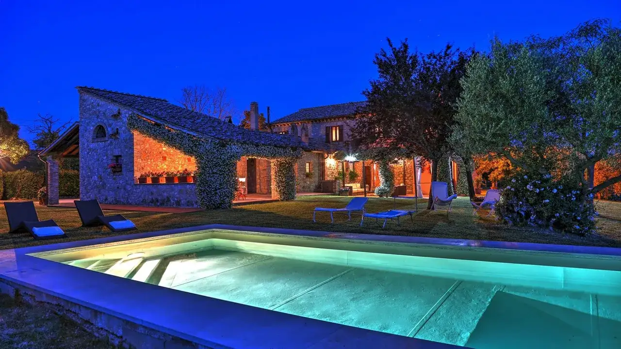 Una splendida masseria in Toscana illuminata di notte, con piscina, lettini e alberi secolari.