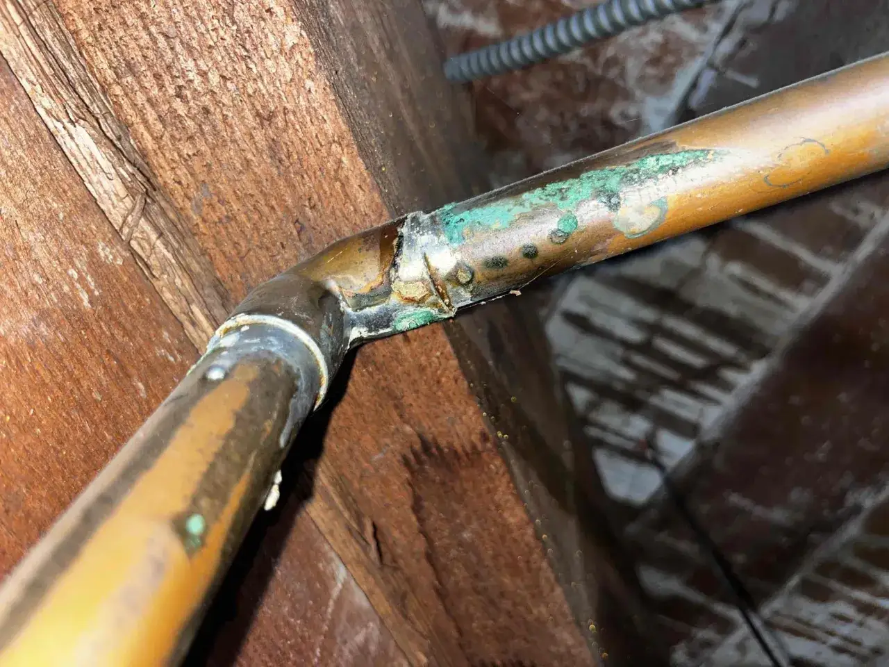 Tuyau en cuivre corrod&eacute;, avec des d&eacute;p&ocirc;ts verts et des traces d'eau, indiquant un danger de fuite.