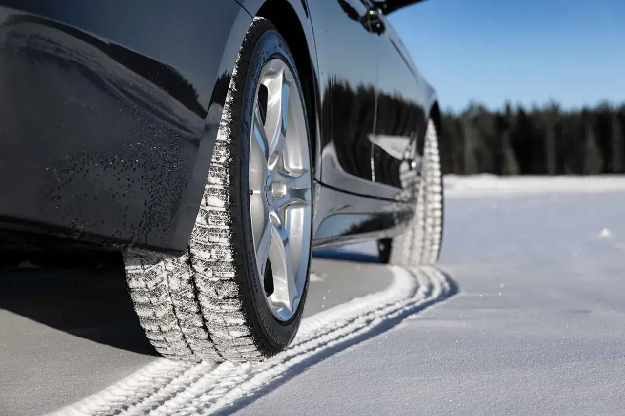 Test opon zimowych SUV na śniegu. Czarne auto z felgami na tle lasu i błękitnego nieba.