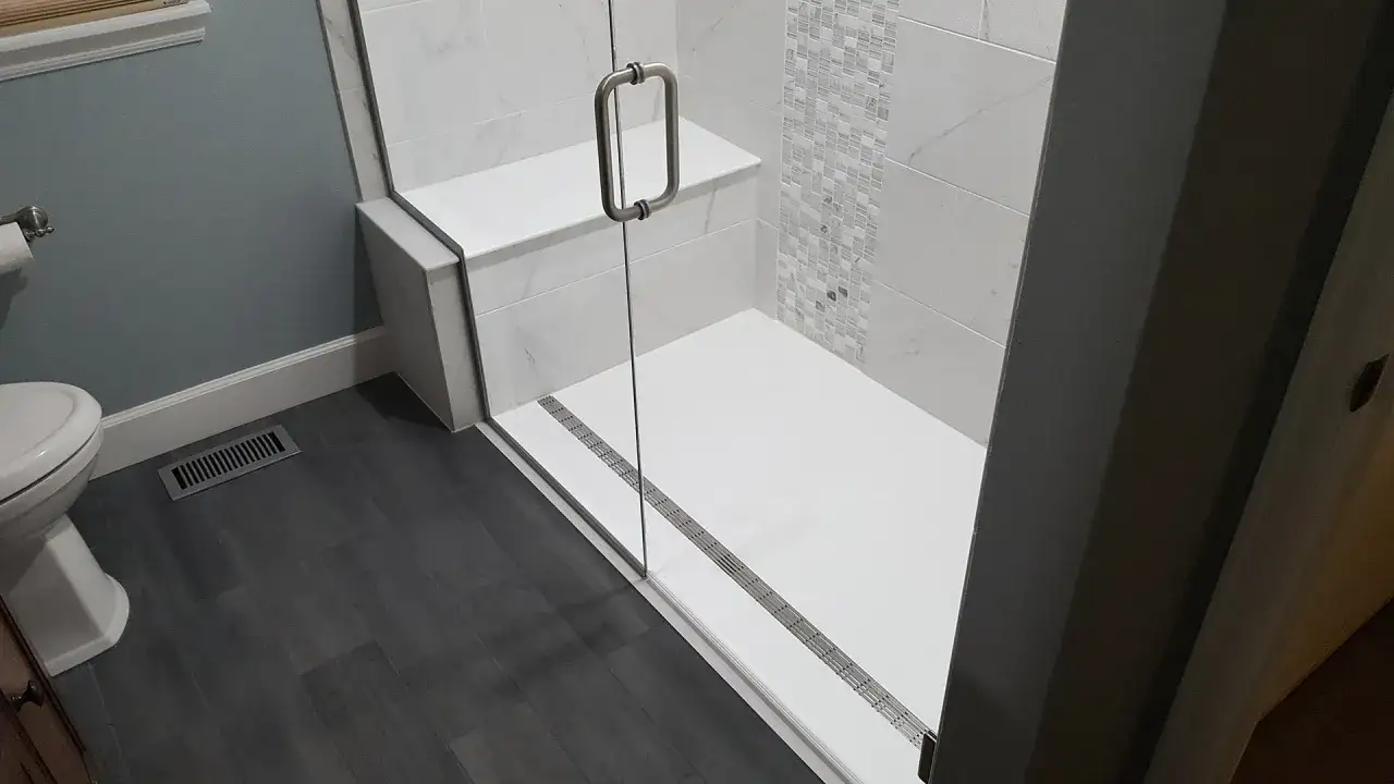 Douche moderne avec banc intégré. Le bac de douche blanc et le carrelage mural créent un espace épuré. Les dimensions du bac de douche sont idéales pour un confort optimal.