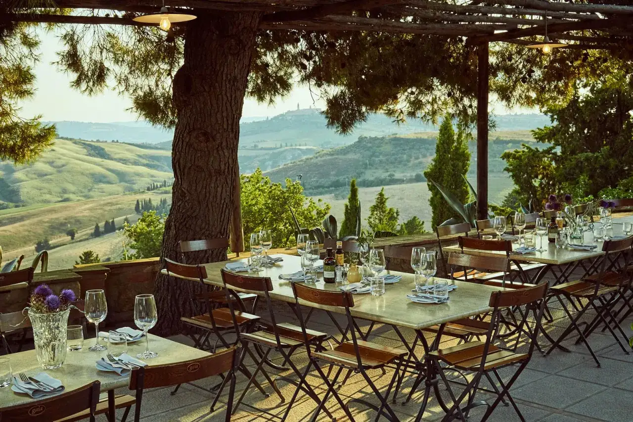 Tavoli apparecchiati sotto un pergolato con vista sulle colline toscane. Perfetto per un pranzo in uno degli agriturismi in Toscana.