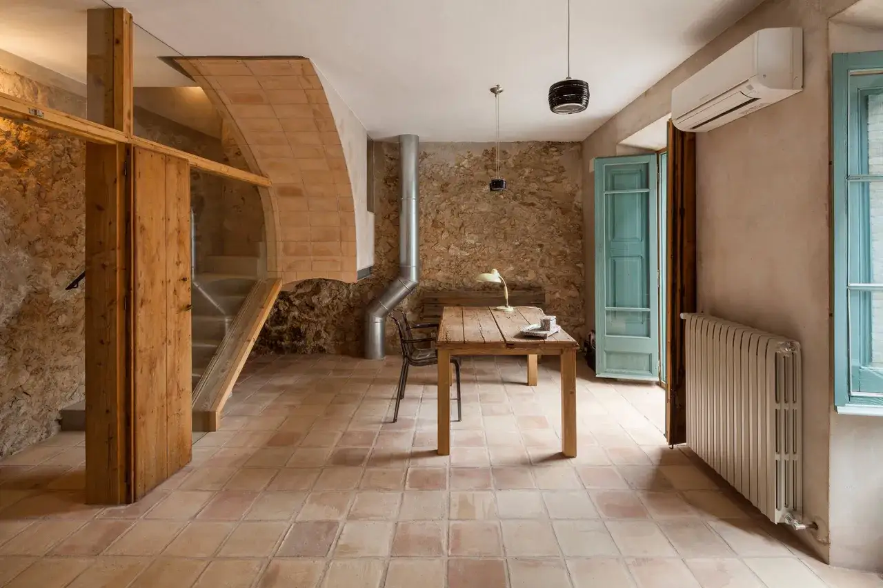 Suelo de **barro cocido** en un espacio rústico con paredes de piedra, escalera de madera y una mesa de trabajo.