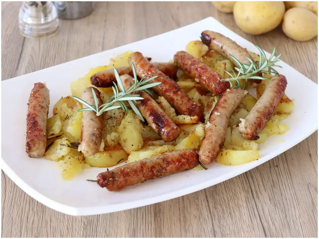 Un piatto invitante di salsiccia e patate arrosto, guarnito con rosmarino fresco.