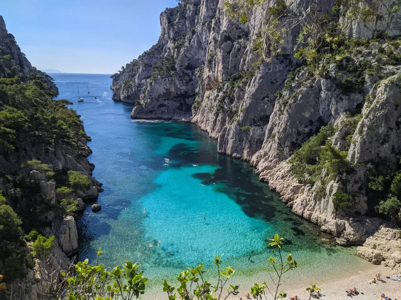 Aguas turquesas y cristalinas en el calanque d'en Vau, rodeado de imponentes acantilados rocosos y vegetaci&oacute;n. Personas nadan y disfrutan de la playa.