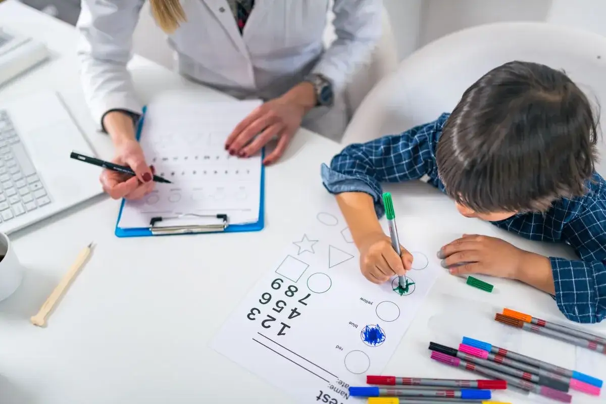 Dziecko wykonuje zadania w ramach diagnozy psychologicznej, rysując kształty i liczby pod okiem psychologa.