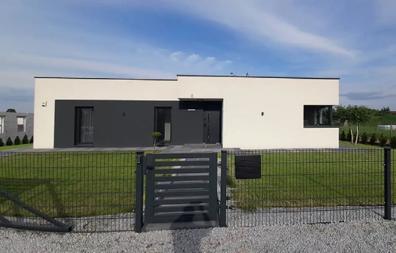 Nowoczesne domy z płaskim dachem parterowe, z białymi i grafitowymi elewacjami, ogrodzone metalowym płotem.