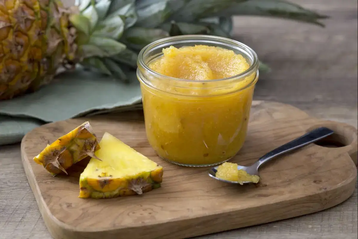 Un pot de confiture d'ananas maison, avec des morceaux d'ananas frais et une cuill&egrave;re remplie de cette d&eacute;licieuse confiture.