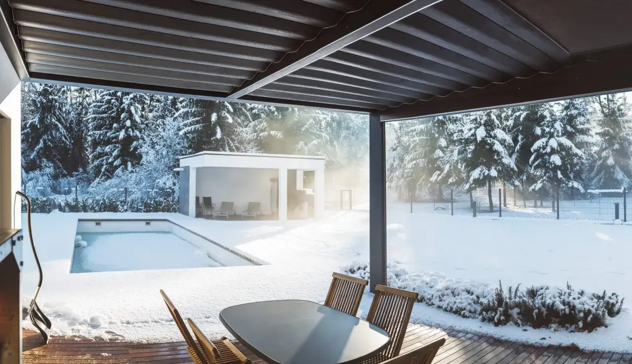 Vinterdag vid poolen. Snö täcker allt utom poolen, som har isolering under poolen. Solen skiner genom träden.