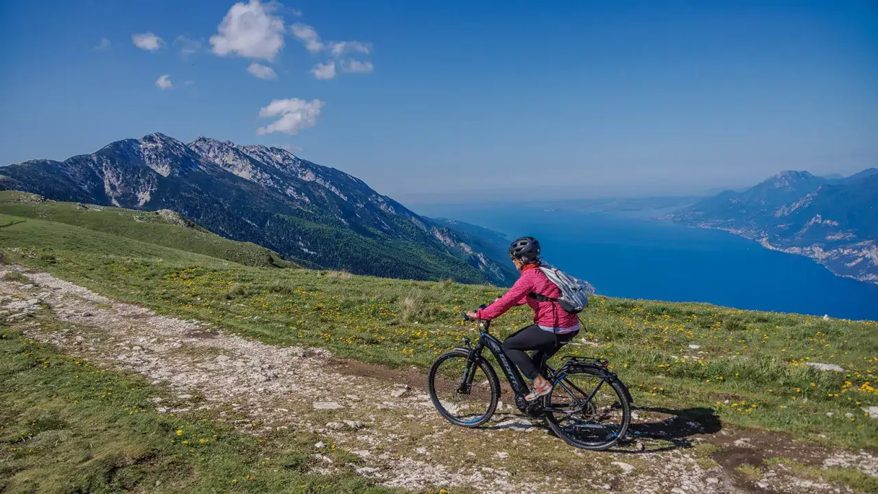 Ciclista su sentiero con vista mozzafiato sul lago di Garda e Monte Baldo.