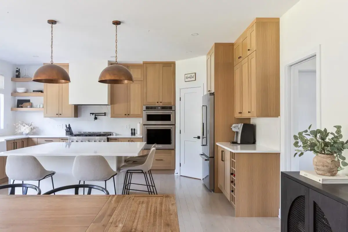 Modern kitchen styling with warm wood cabinets, a large white island, and copper pendant lights.