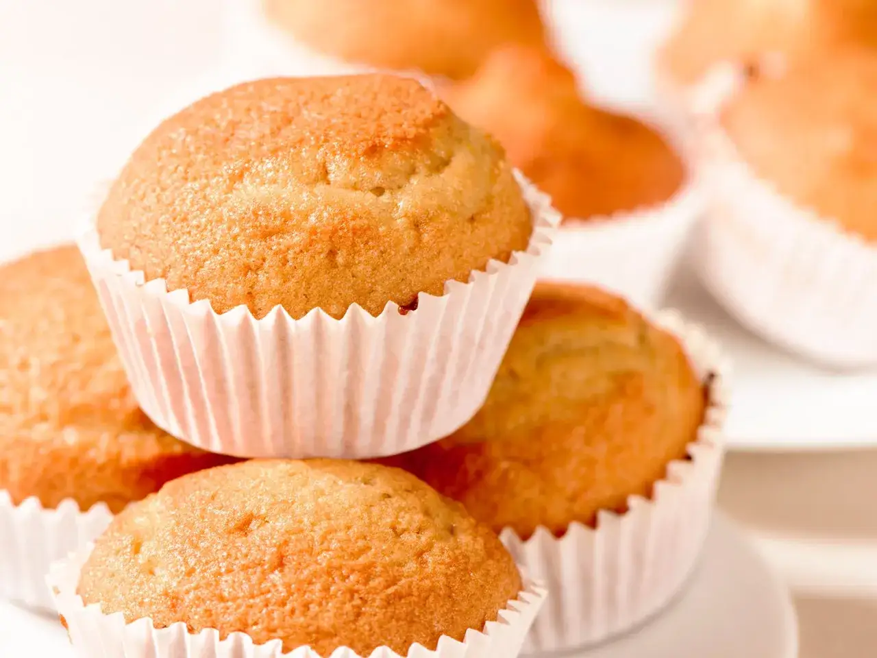 Goldbraune, fluffige vegane Muffins in weißen Papierförmchen, gestapelt und bereit zum Genießen.