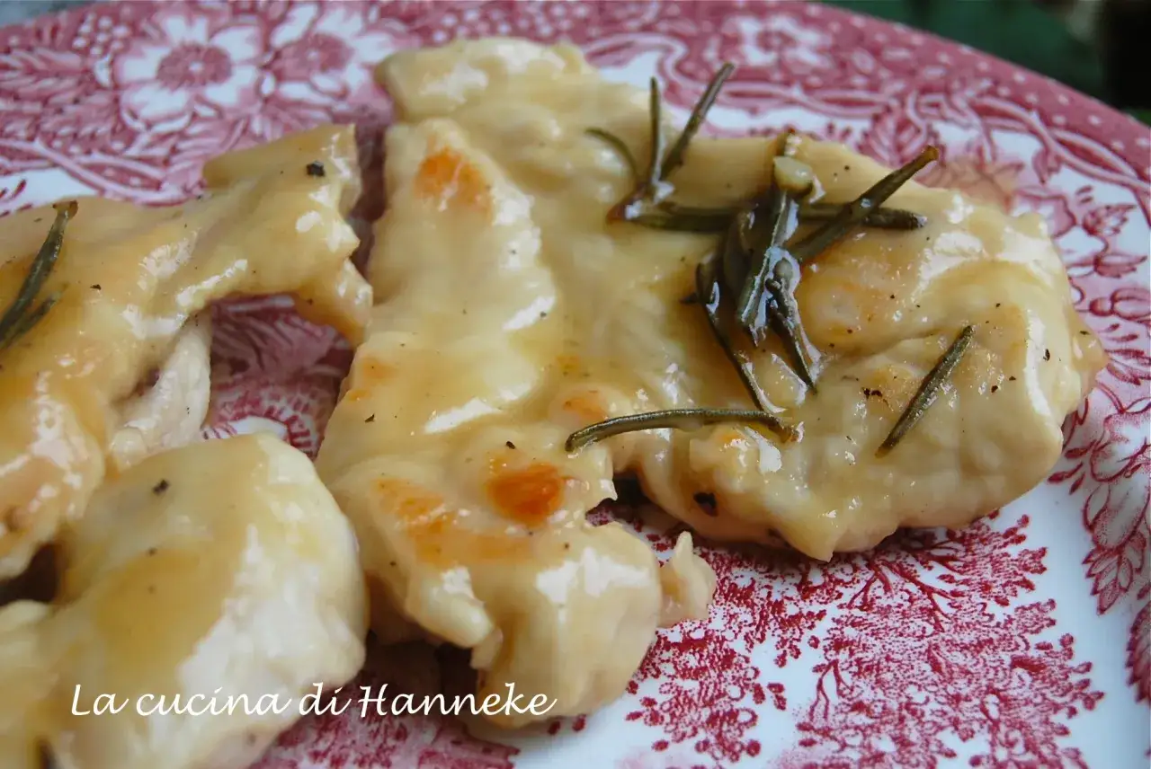 Petto di pollo in salsa cremosa con rosmarino, servito su un piatto rosso e bianco.