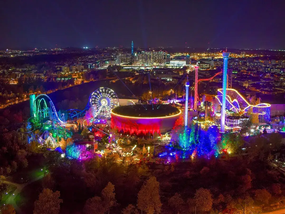 Nattbild &ouml;ver ett upplyst tivoli i Helsingfors med berg-och-dalbanor, pariserhjul och torn.