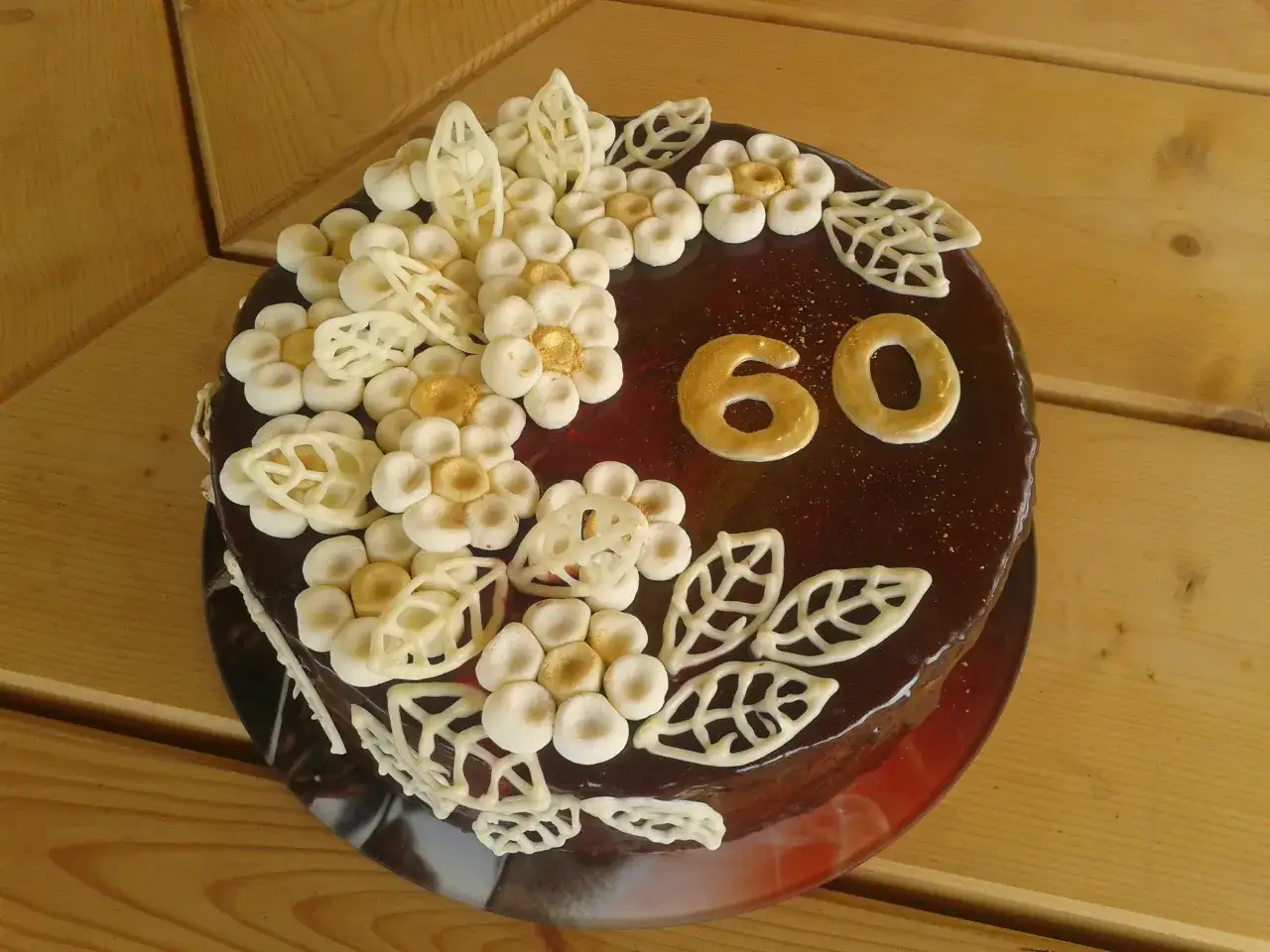 Elegancki tort na 60 urodziny dla mamy, ozdobiony czekoladowymi kwiatami i złotymi cyframi.