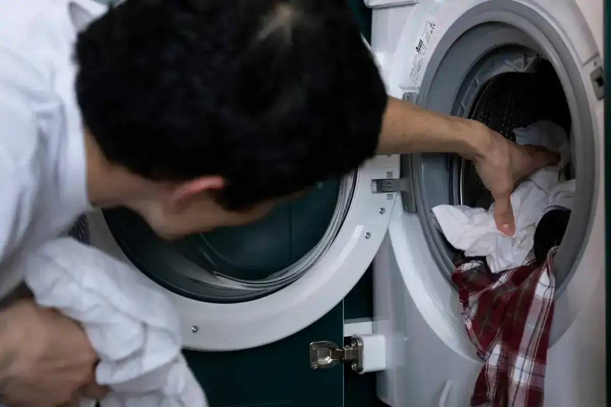 Hombre mete ropa a lavadora para blanquear ropa blanca con bicarbonato.