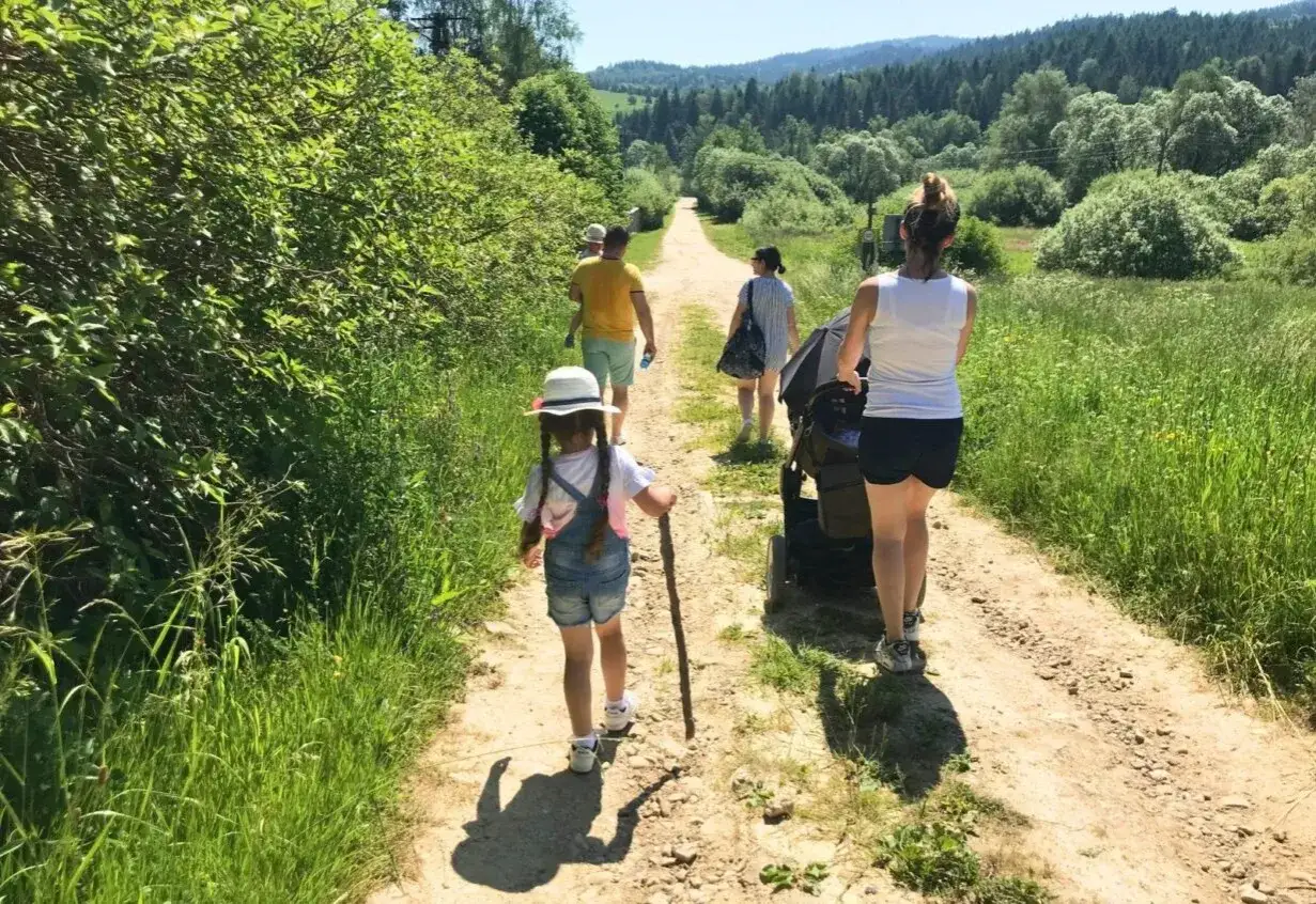Rodzina spaceruje po ścieżce w Beskidzie Śląskim. Mała dziewczynka z patykiem w ręku idzie przodem, a za nią rodzice z wózkiem.