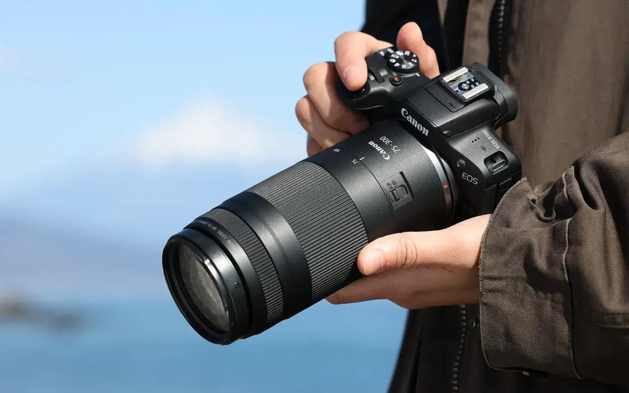 Dłoń trzyma aparat Canon z obiektywem 75-300, idealnym do fotografii przyrodniczej i sportowej.