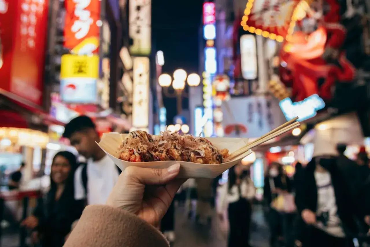 Pyszne takoyaki na talerzyku, idealne do spróbowania, gdy zastanawiasz się, co warto zobaczyć w Tokio. Tętniące życiem nocne uliczki w tle.