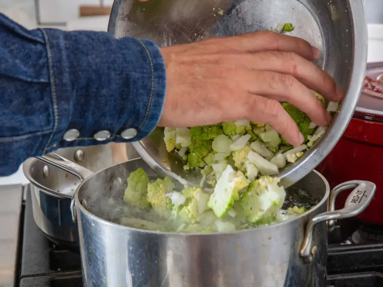 Ręka wsypuje do gotującej wody pokrojony brokuł romanesco.