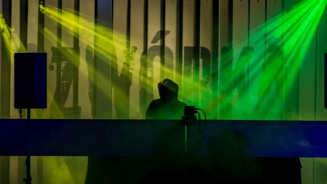 Artysta w kapturze na scenie, oświetlony zielonymi i żółtymi światłami. Tło z logo, sugerujące koncert **tonfa rap**.