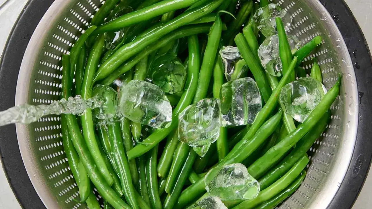Grüne Bohnen werden in einem Sieb mit Eiswasser abgeschreckt, um das **Bohnen blanchieren** zu stoppen und ihre Farbe zu erhalten.