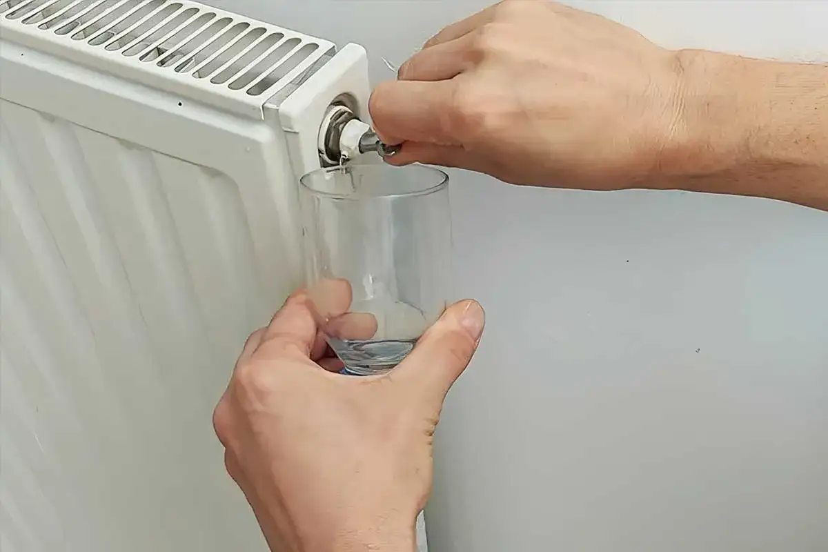 Une personne purge un radiateur, capturant l'eau qui coule dans un verre. Le bruit de l'eau qui coule est audible.