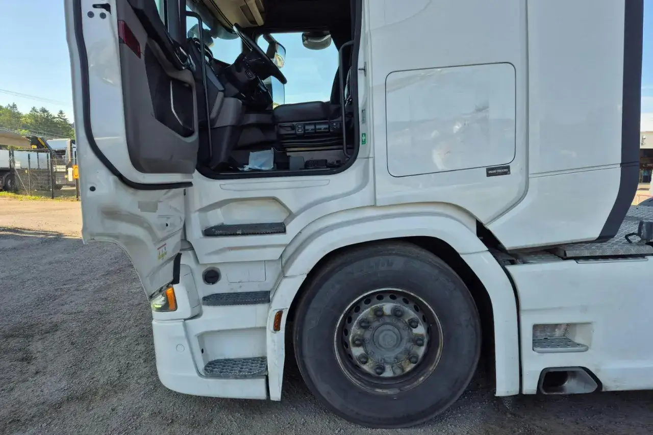 Vitt chassi p&aring; en begagnad Scania lastbil med &ouml;ppen d&ouml;rr. Syns framhjul, trappsteg och del av f&ouml;rarhytten.