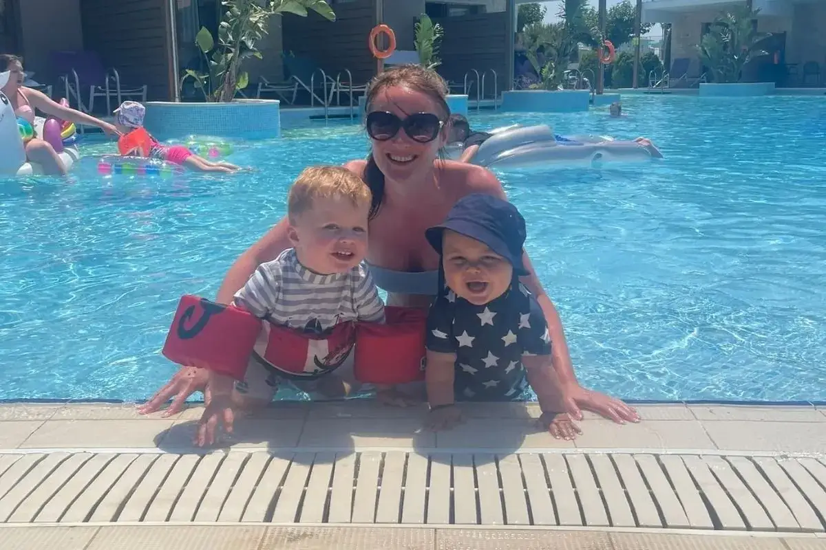 Glückliche Familie im Pool, ein magischer TUI Magic Life Plimmiri Urlaub. Zwei kleine Kinder mit Schwimmflügeln und eine Frau genießen das Wasser.