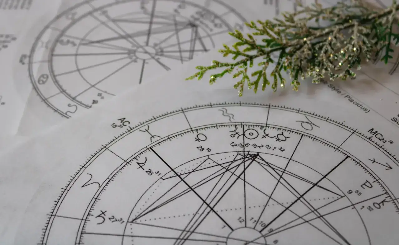 Dwa wykresy astrologiczne, jeden z nich z symbolem 2. domu, leżą obok siebie. Gałązka iglaka z brokatem dodaje świątecznego nastroju.