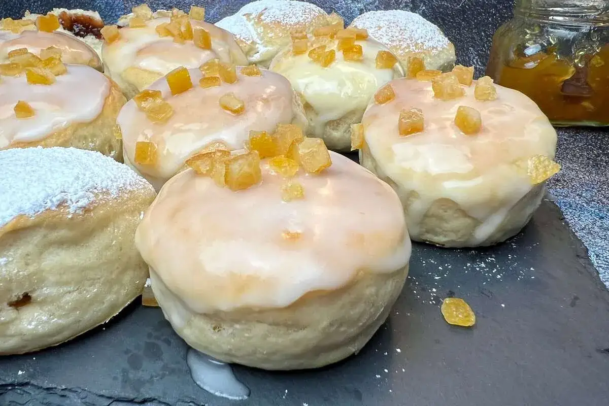 Pyszne pączki z piekarnika, polane lukrem i posypane kandyzowanymi skórkami pomarańczy. Niektóre oprószone cukrem pudrem.