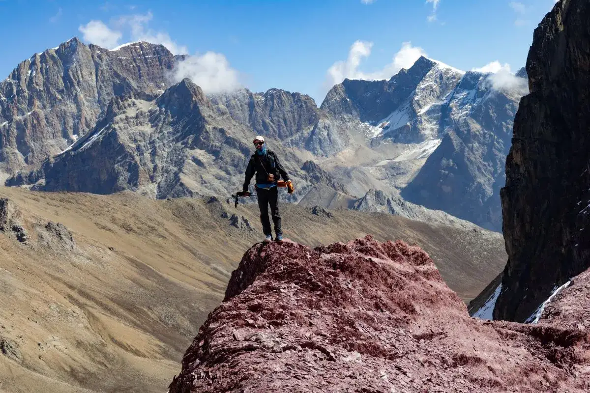 Jérémy Bigé, un alpiniste, se tient au sommet d'une crête rocheuse rouge, dominant un paysage montagneux spectaculaire sous un ciel bleu.