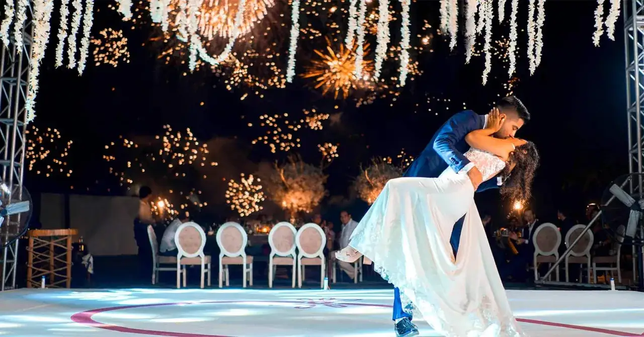Una coppia si bacia durante un ballo, con fuochi d'artificio che illuminano il cielo notturno. Un'idea di intrattenimento matrimonio davvero originale e romantica.