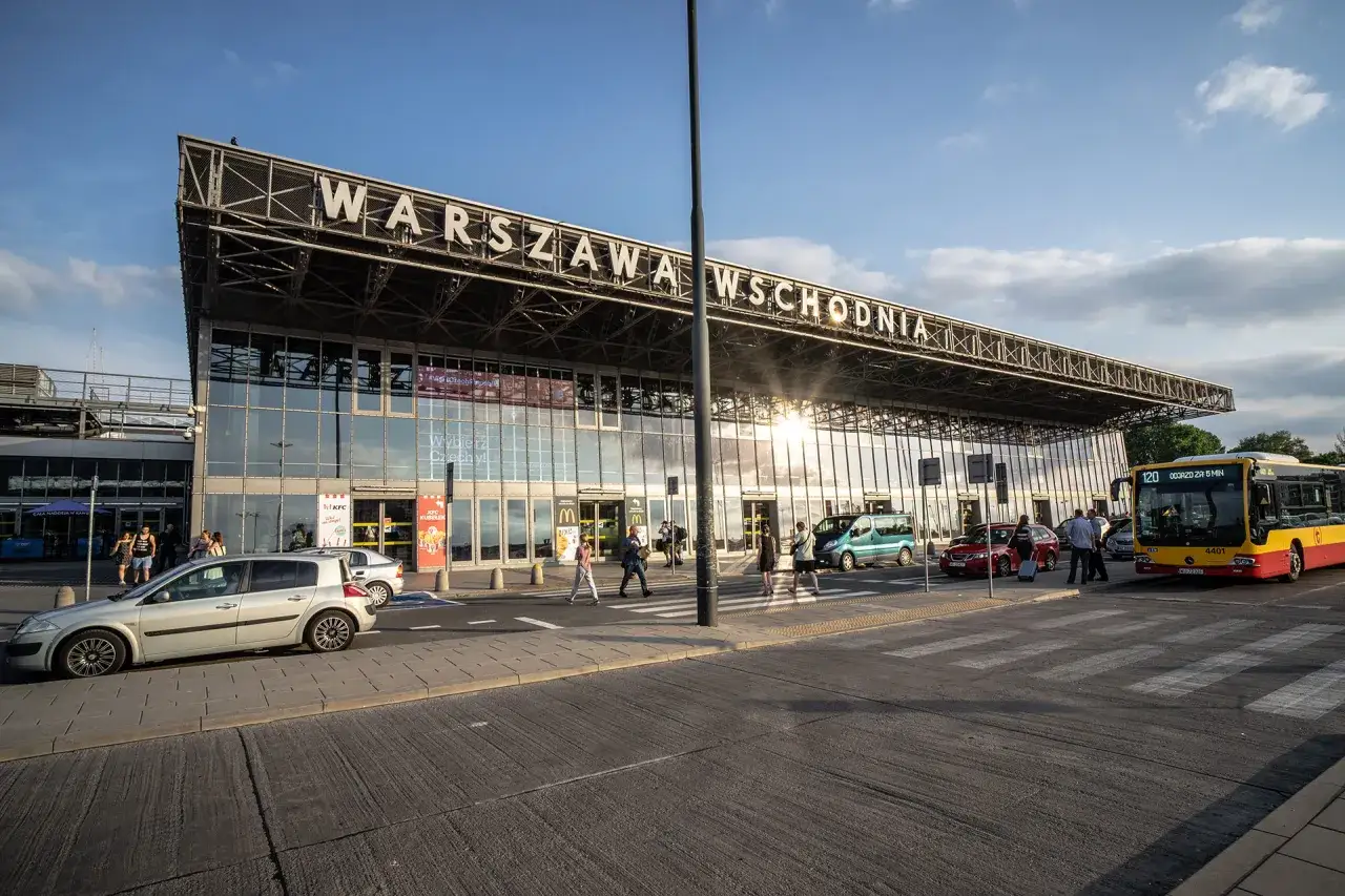 Warszawa Wschodnia, dworzec autobusowy, gdzie czeka żółty autobus. Słońce odbija się w szklanej fasadzie.