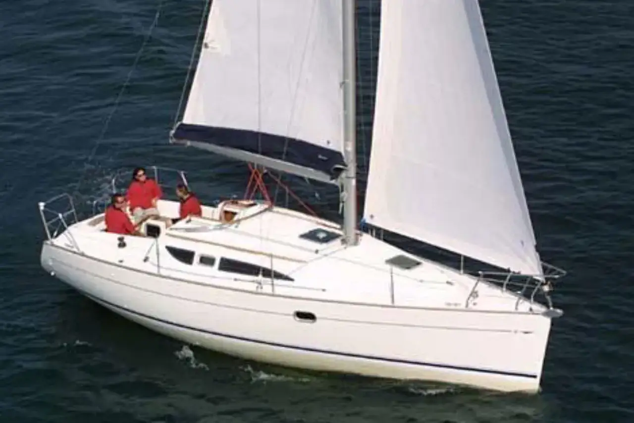 Un voilier blanc, un Sun Odyssey 32i, navigue sur une mer bleue avec trois personnes à bord.