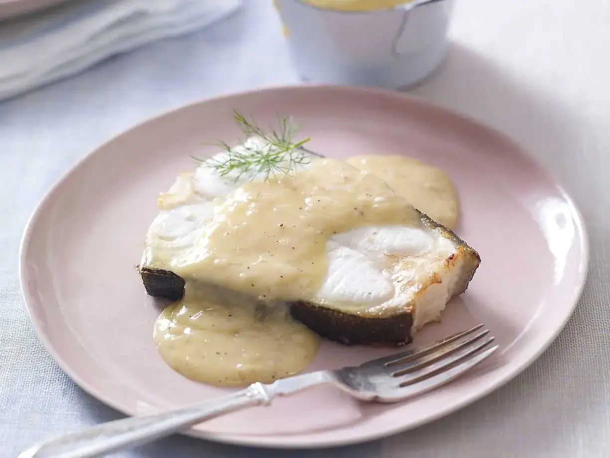 En bit fisk med kr&auml;mig s&aring;s, som p&aring; en mysig cafe de Paris. Serveras p&aring; en ljusrosa tallrik med en gaffel.