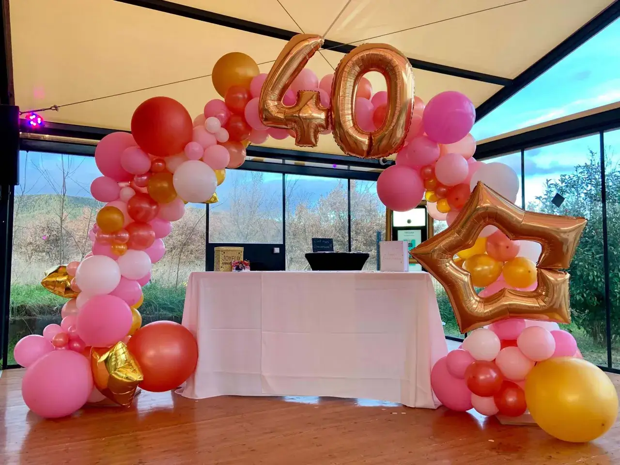 Décoration festive pour un 40ème anniversaire avec une arche de ballons roses, corail et dorés, incluant des chiffres