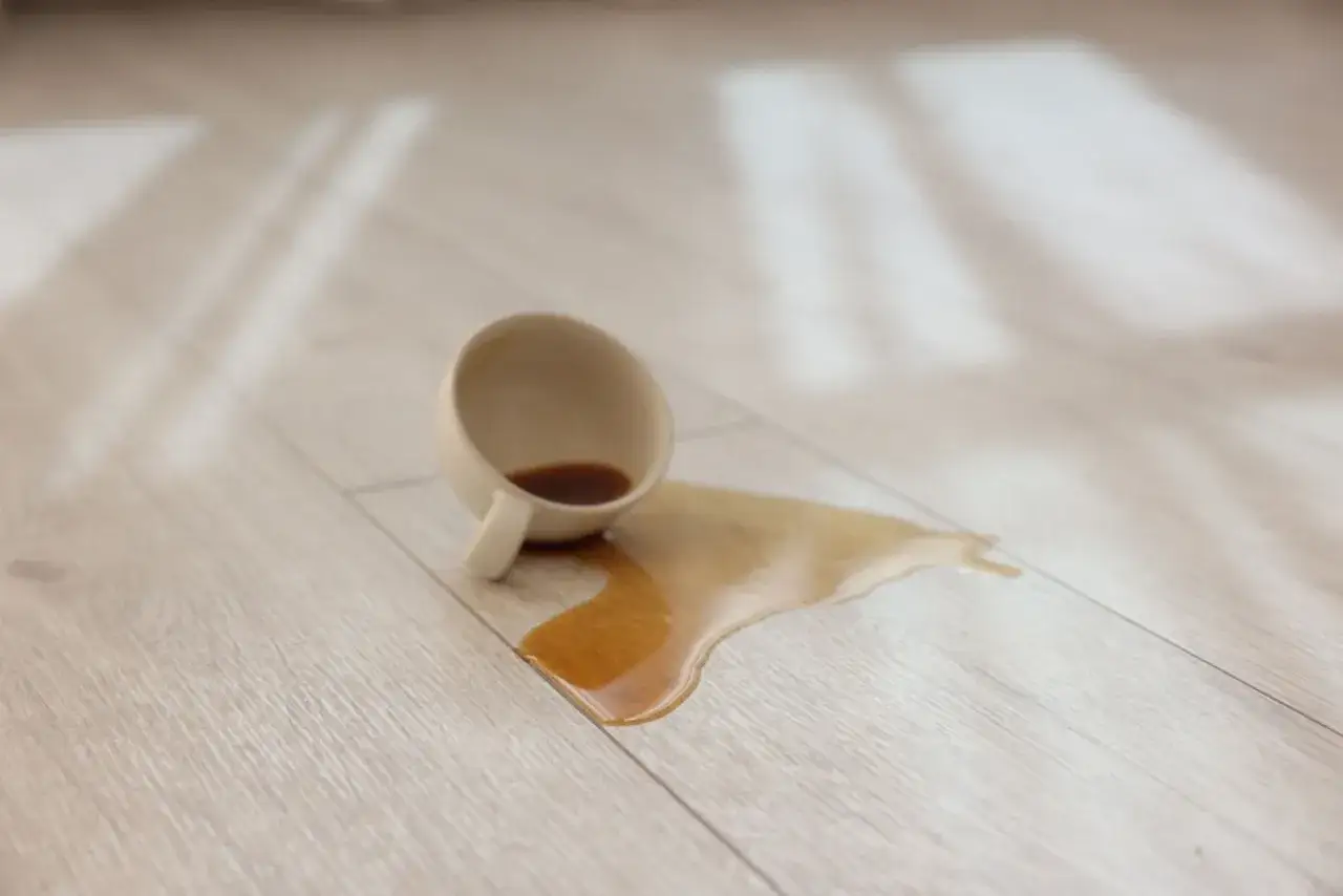 Taza volcada con caf&eacute; derramado sobre suelo de madera. C&oacute;mo quitar mancha negra humedad madera.