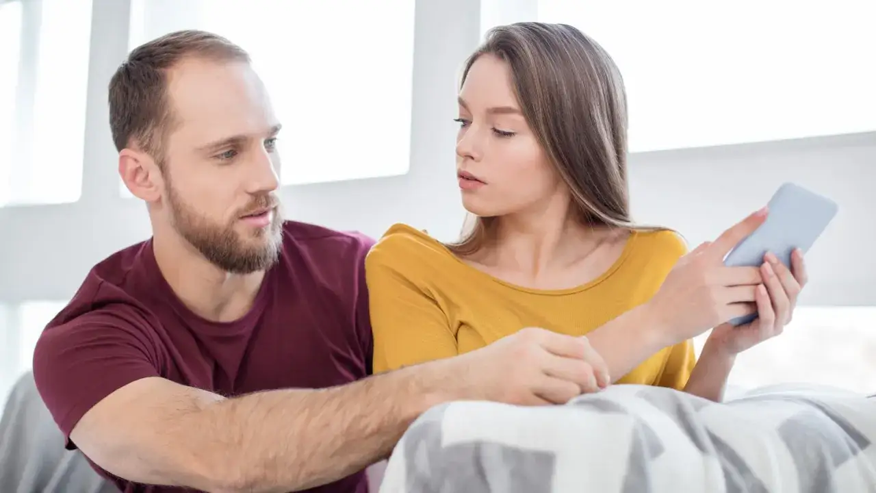 Una ragazza guarda il telefono con espressione preoccupata, mentre il suo ragazzo le mette una mano sulla spalla, forse per consolarla o forse perché anche lui è turbato dal fatto che il mio ragazzo mette like alle altre.