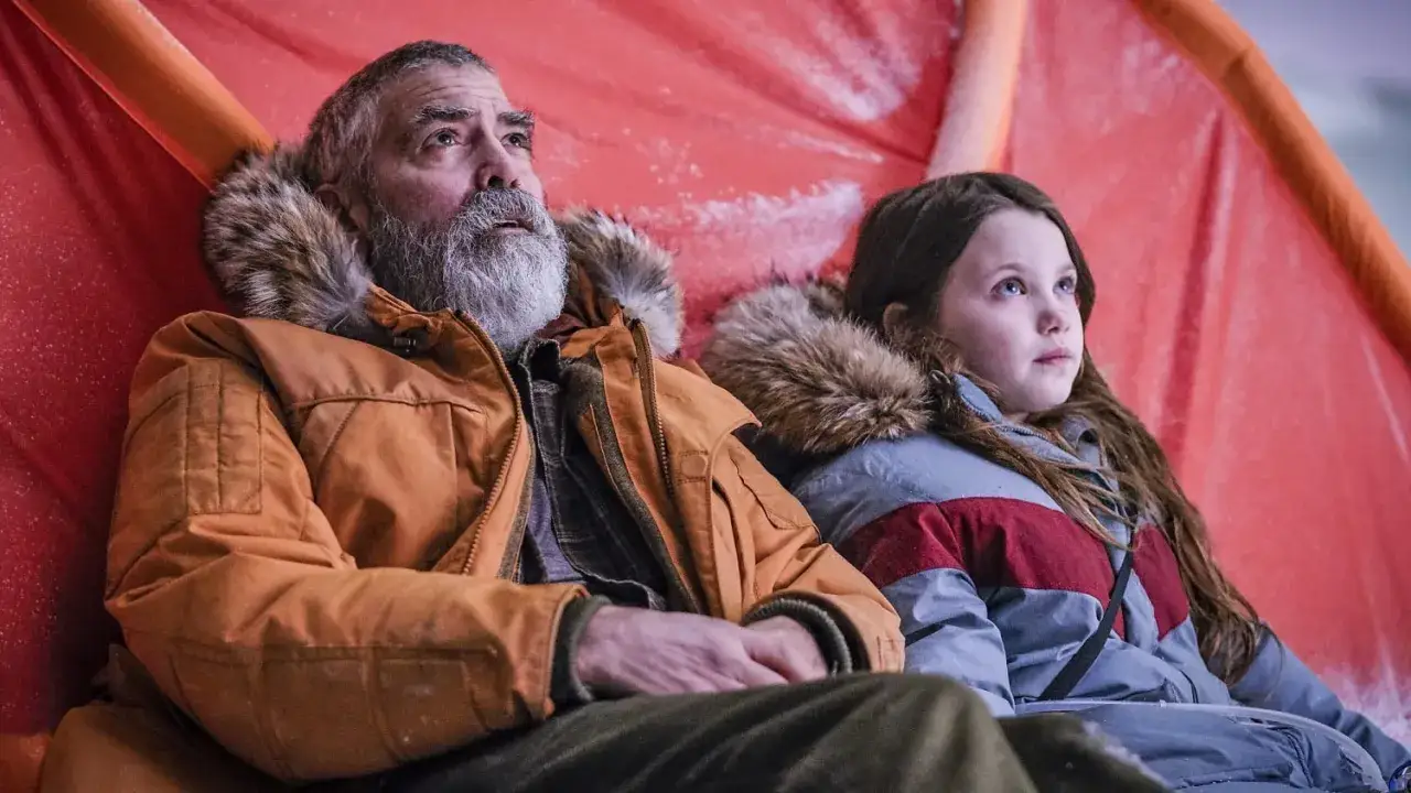 George Clooney i dziewczynka w zimowych kurtkach patrzą w górę, jakby wypatrywali gwiazd na niebie o północy.