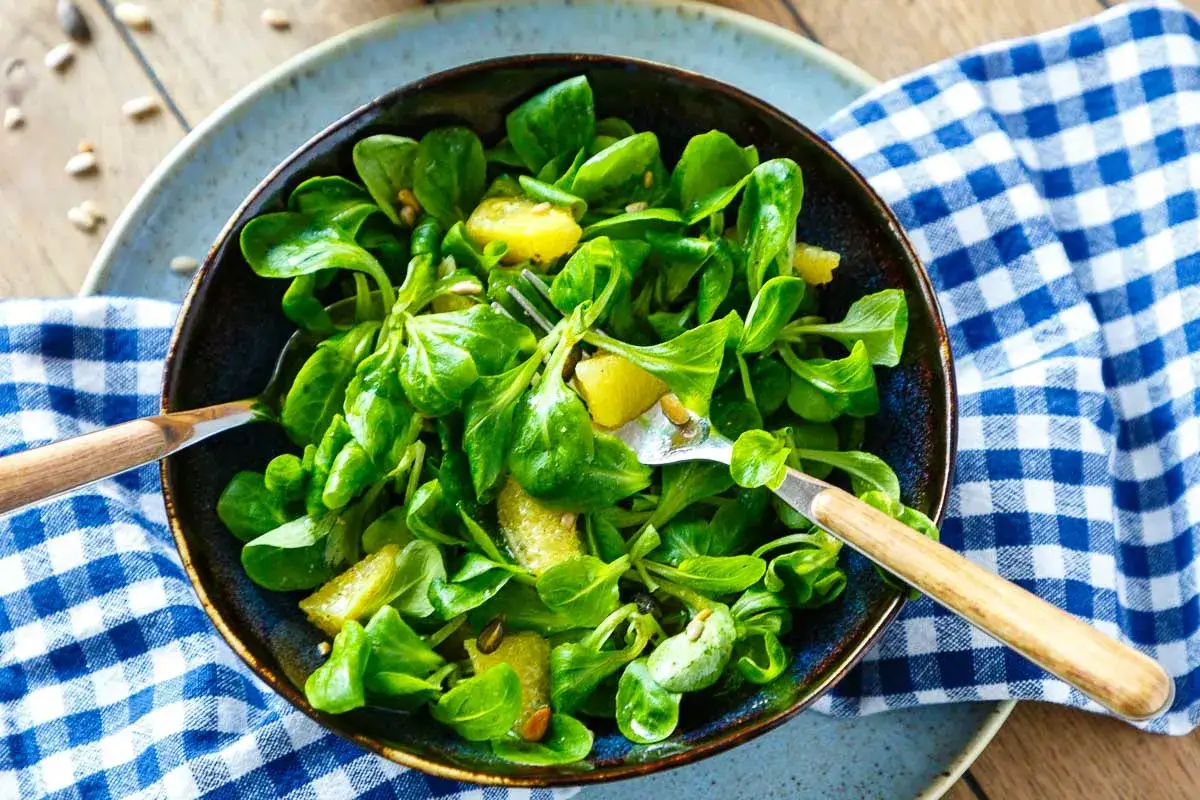 Ein frischer Wintersalat mit saftigen Orangenspalten und knackigen Kernen, serviert in einer Schüssel mit Holzgabel und Löffel.
