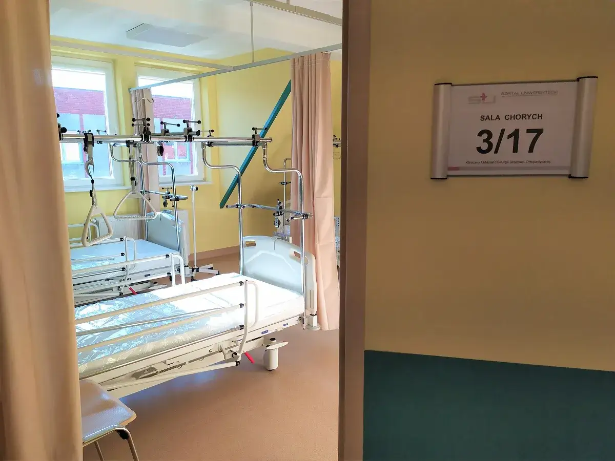 Szpitalna sala chorych z łóżkami i aparaturą medyczną.