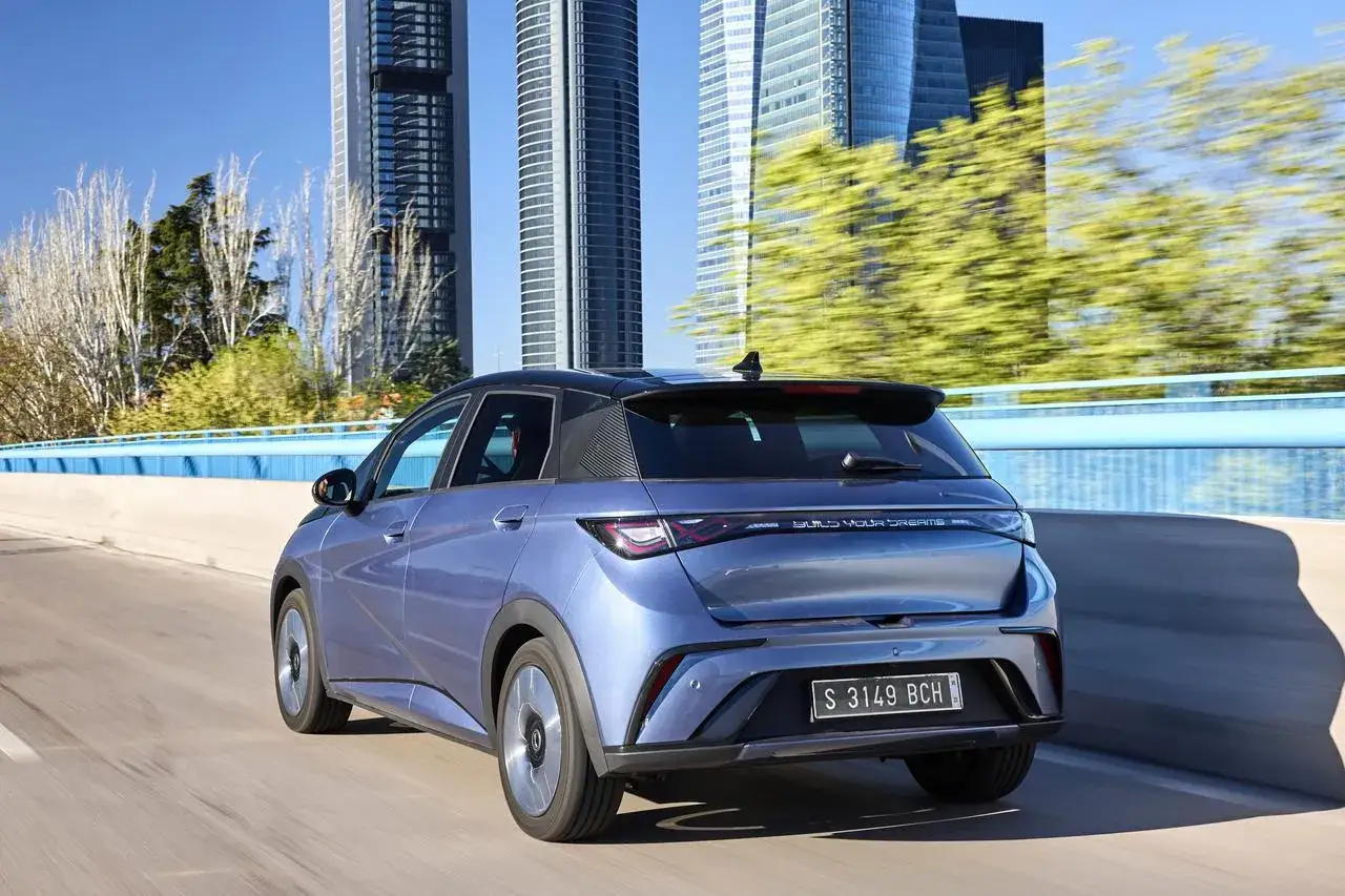Auto elettriche pi&ugrave; vendute: una berlina blu metallizzato sfreccia su un ponte con grattacieli sullo sfondo.