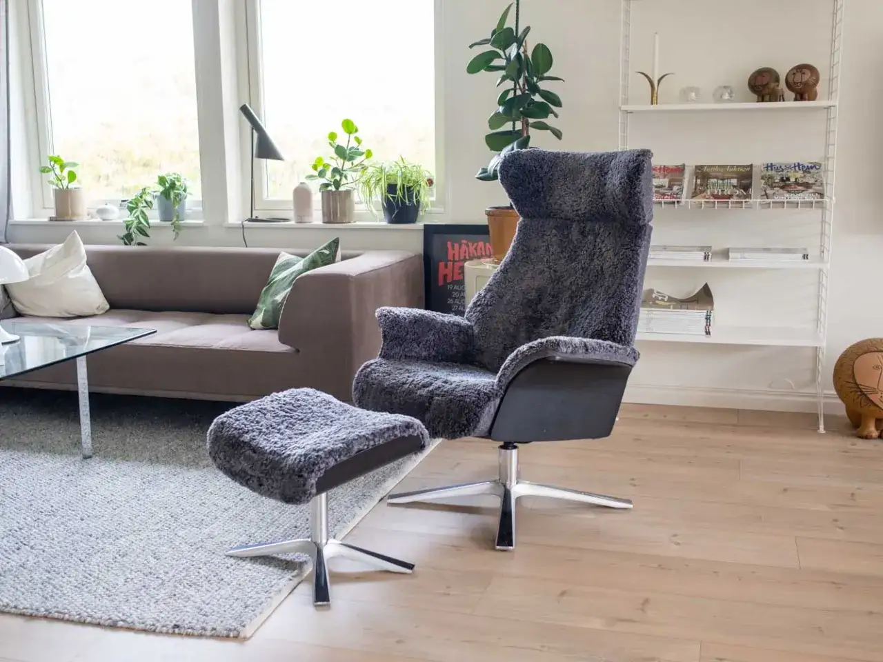 En bekv&auml;m f&aring;t&ouml;lj med f&aring;rskinn och fotpall ger en k&auml;nsla av conform air i vardagsrummet. En soffa och bokhylla syns i bakgrunden.