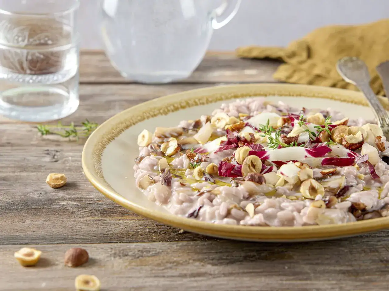 Un cremoso risotto al radicchio, guarnito con nocciole tostate e un rametto di timo fresco, su un piatto rustico.