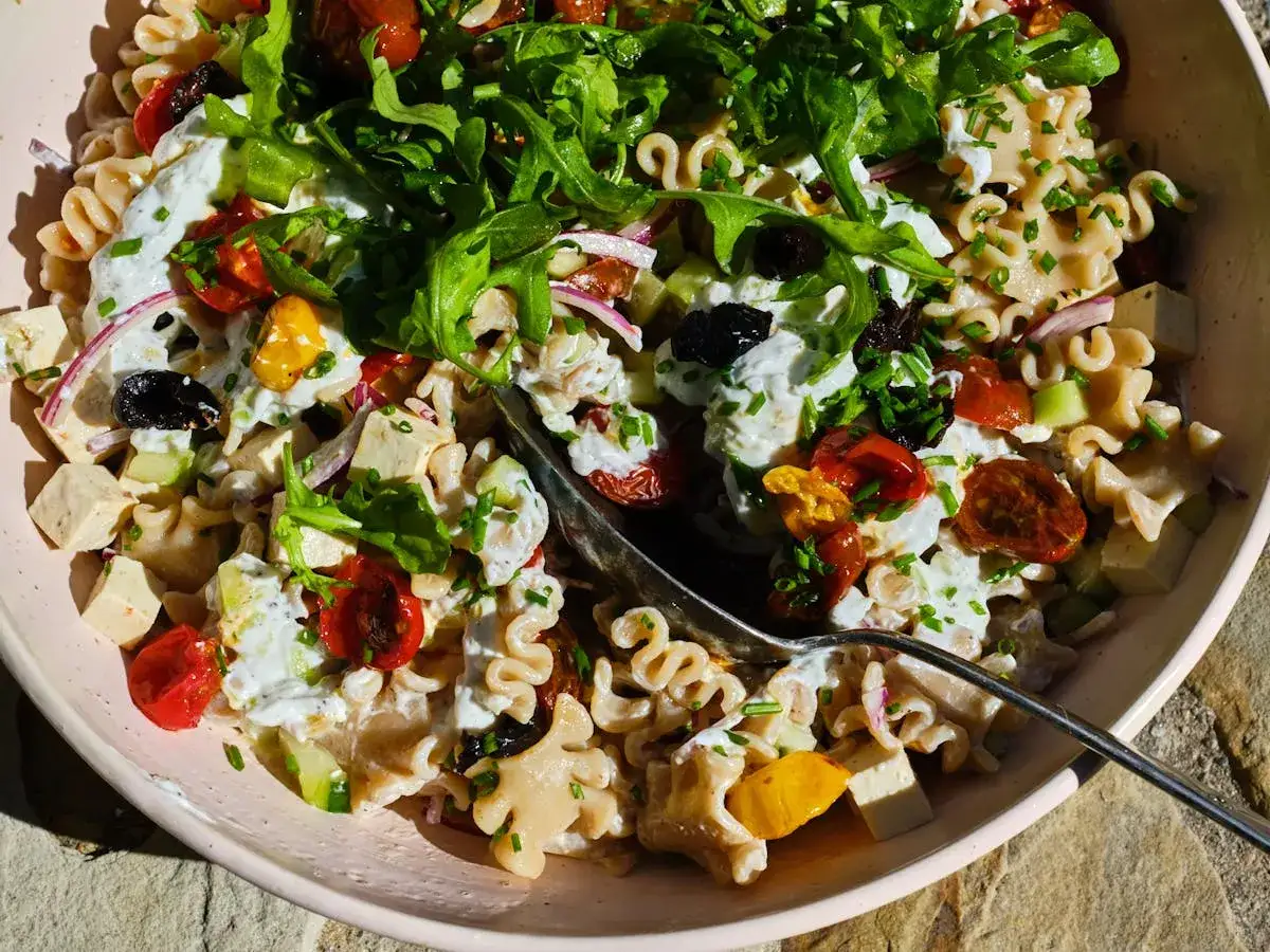Ein bunter mediterraner Nudelsalat mit Rucola, Tomaten, Oliven und Feta. Perfekt für einen sonnigen Tag!