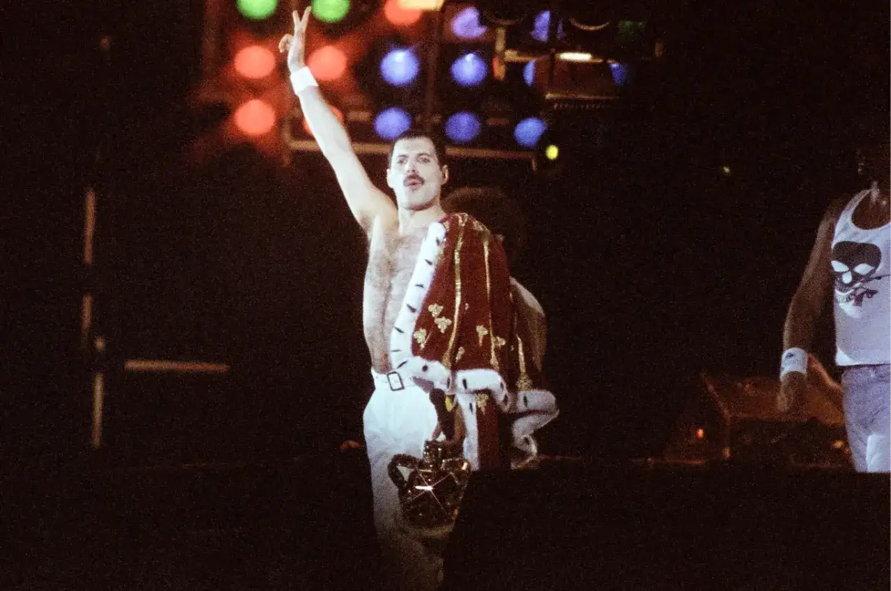 Freddie Mercury, w koronie i płaszczu, pozdrawia publiczność. To mógł być jego ostatni koncert.