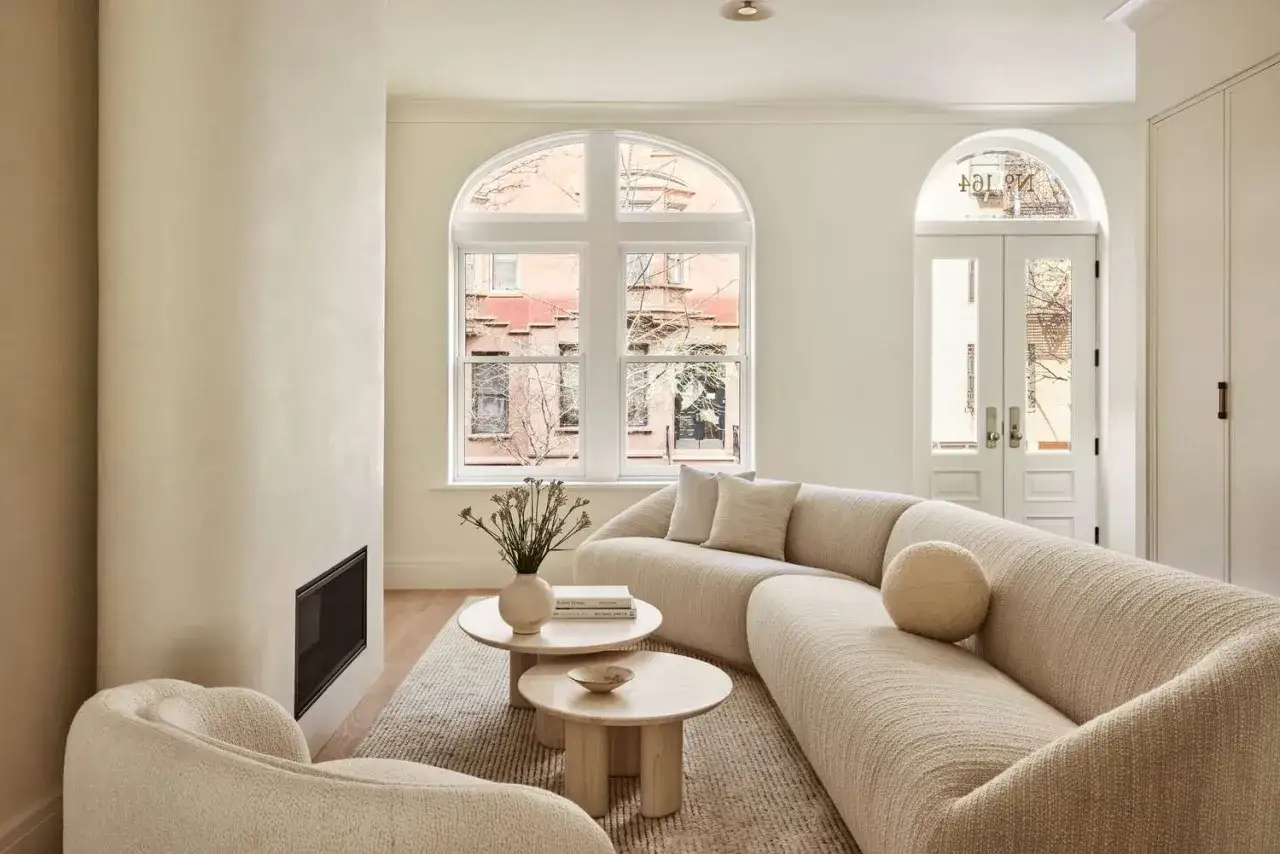 Ein helles, modernes Wohnzimmer gestalten mit einem geschwungenen Sofa, runden Couchtischen und einem Kamin. Große Bogenfenster lassen viel Licht herein.