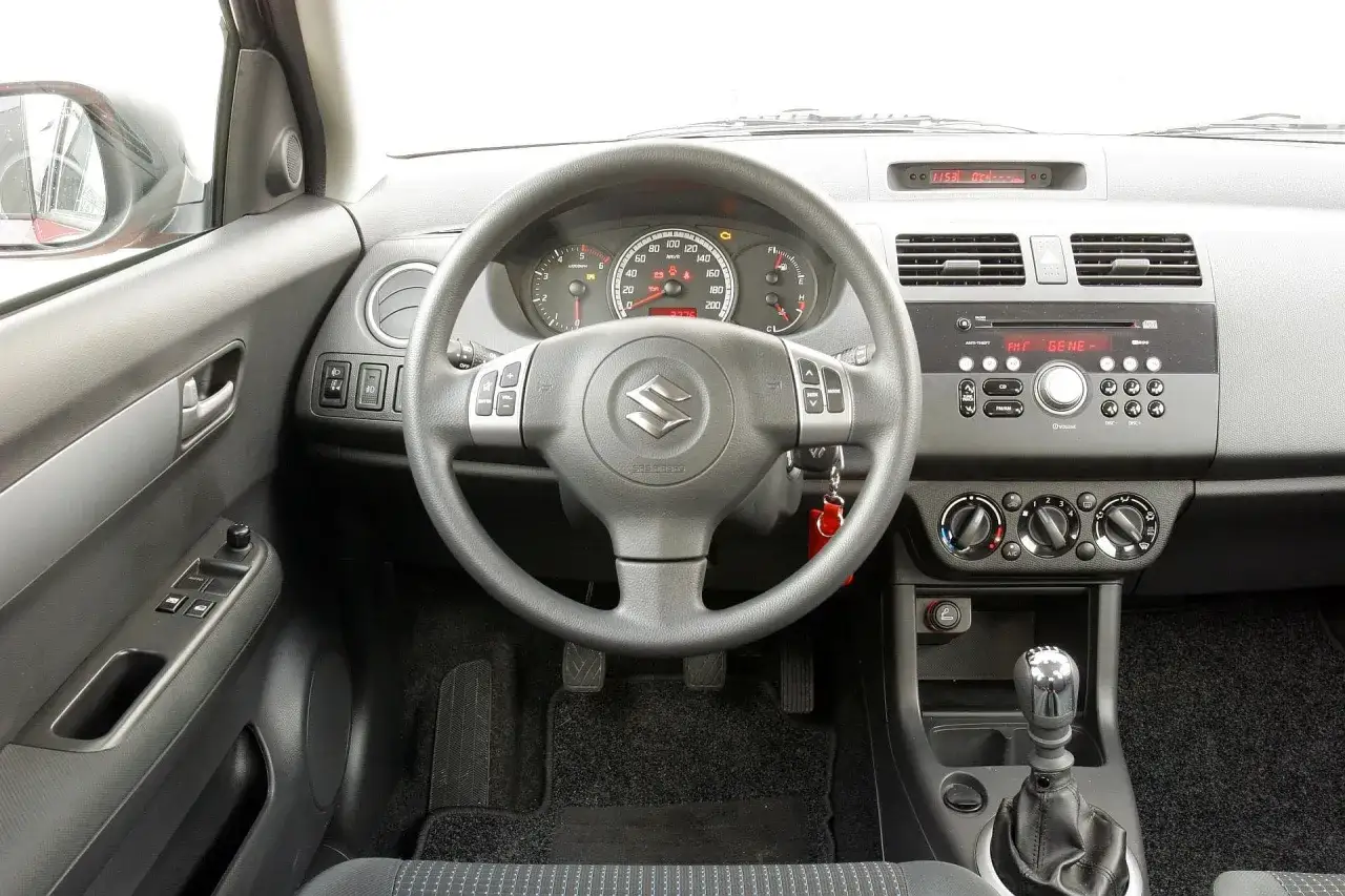 Wnętrze Suzuki Swift 2007: kierownica, deska rozdzielcza z radiem i zegarami, dźwignia zmiany biegów.