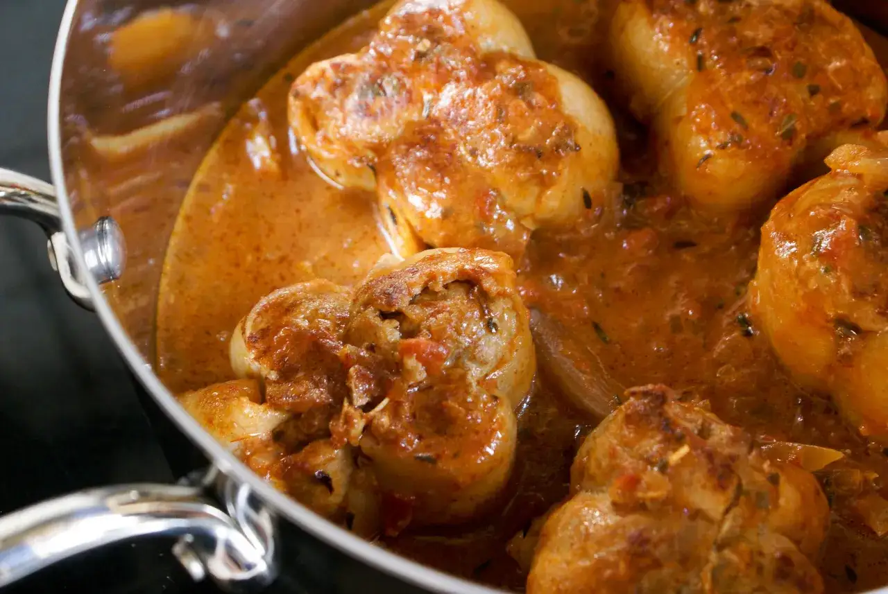Paupiettes de veau mijotant dans une sauce tomate et herbes, dans une cocotte en m&eacute;tal.